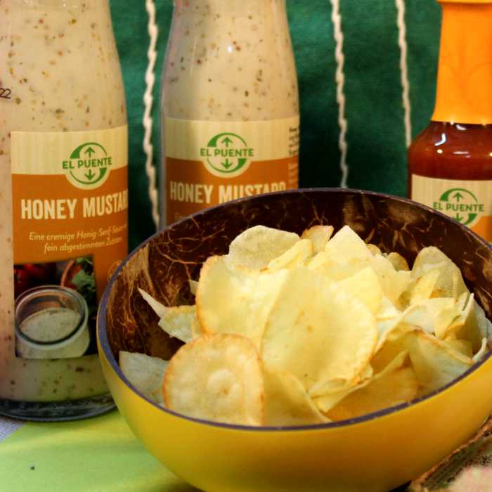 Eine Schale mit Kartoffelchips steht vor Flaschen mit Salatsaucen von El Puente