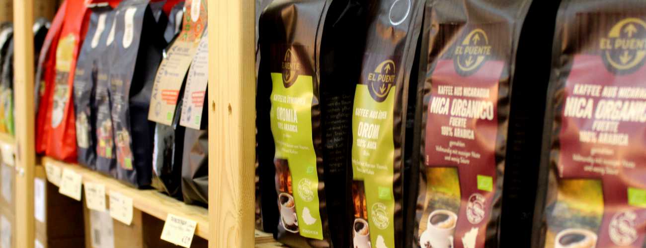 Viele schwarze Tüten mit Fair Trade-Kaffe von El Puente stehen in einem Holzregal