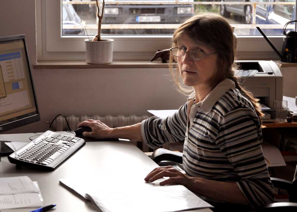 Eine Frau mit Brille sitzt am Schreibtisch und arbeitet am Computer